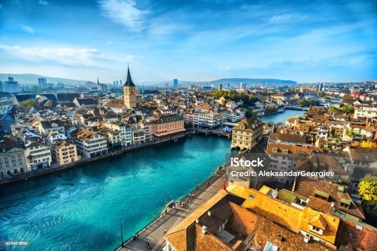 Aerial view of Zurich, Switzerland. Taken from a church tower overlooking the Limmat River. Beautiful blue sky with dramatic cloudscape over the city. Visible are many traditional Swiss houses, bridges and churches.