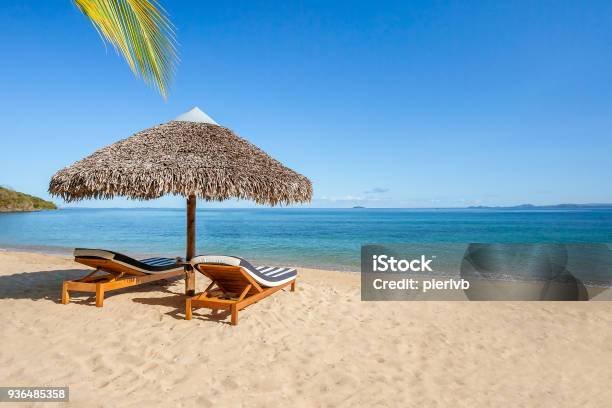 Two sunbeds under a straw umbrella on the tropical beach of Nosy Be, Madagascar